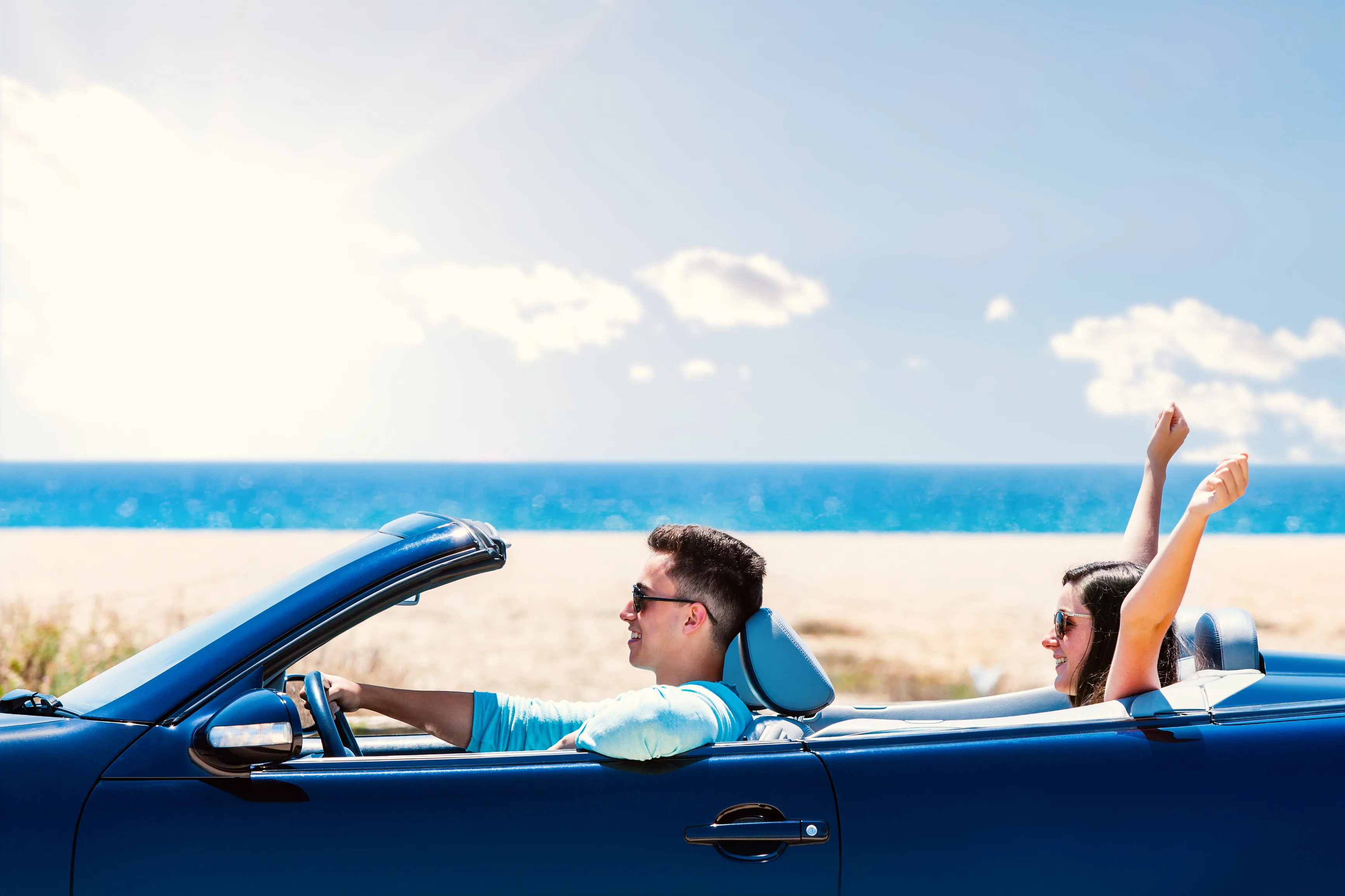 Young adults driving a convertible near the water on a sunny day